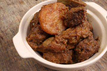 Asian style Beef bhuna dry curry with potato in ceramic bowl over rustic wooden background