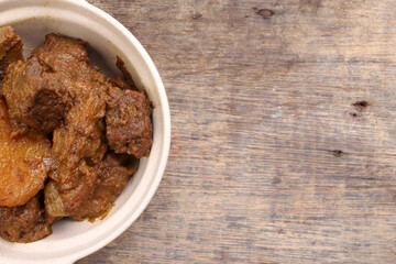Asian style Beef bhuna dry curry with potato in ceramic bowl over rustic wooden background