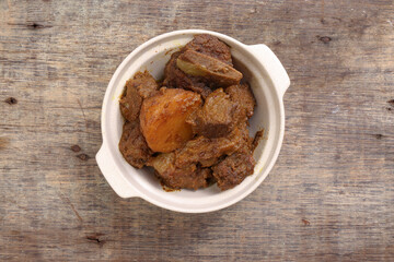 Asian style Beef bhuna dry curry with potato in ceramic bowl over rustic wooden background