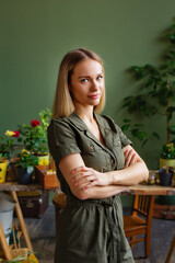 Selective focus. Portrait of a young blonde woman in a khaki jumpsuit on a background of green house plants. Gardening concept.