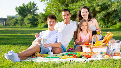 Portrait of happy family with two children enjoying picnic on green meadow together