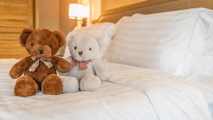 Lovely couple bear sit on white and big bed in bedroom , clean and white blanket with two pillows,hotel room,holidays concept,selective focus,copy space.