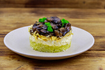 Tasty layered salad with roasted mushrooms, potato, eggs, cheese and mayonnaise on wooden table