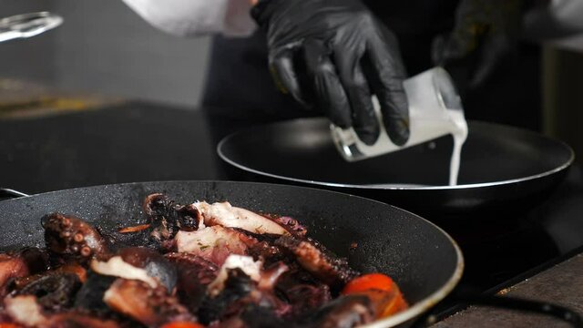 Luxury restaurant. ooking octopus. Pouring milk on frying pan. Cook octopus. Traditional Mediterranean cuisine. Seafood. Chef in black gloves in restaurant kitchen. 4 k video