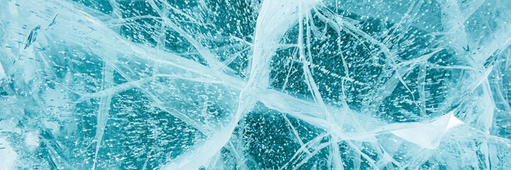 Texture of beautiful blue ice with cracks and air bubbles in the frozen lake. Winter nature background. Banner.