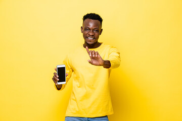 Young smiling African man holding mobile phone and doing no gesture in yellow isolated studio background