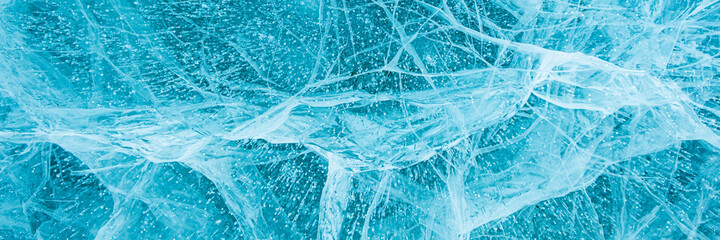 Texture of beautiful blue ice with cracks and air bubbles in the frozen lake. Winter nature background. Lake Baikal, Siberia, Russia. Banner.