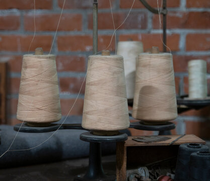 Three large vintage spools of cotton thread featured in an industrial setting with a brick wall in the background