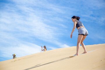 A teenage girl is sandboarding down the sand dune at  Anna Bay Australia.