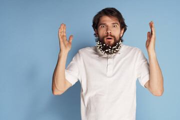 Emotional man in a white T-shirt flowers in a beard blue background