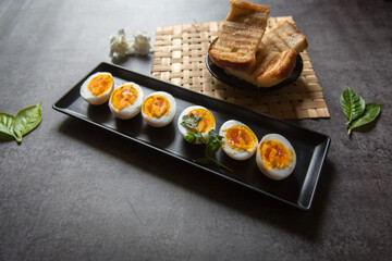 Boiled egg slices in a tray and breads on a dark background.