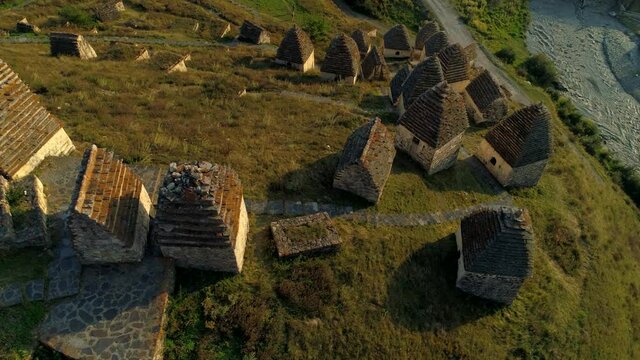 Drone top down cinematic roofs of houses Dargavs North Ossetia ancient semi-underground crypts, city of dead famous traditional alpine burial ground. Caucasus Russia landmark. Mountain river. Summer