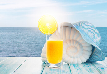 Summer holiday background. Fresh orange juice, orange slice, hat, shell on a wooden table on the background of the sea. Summer vacation concept. Copy space.