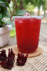 Iced roselle tea glass with fresh roselle fruit on wooden table for healthy herbal drink concept.