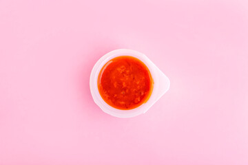 Red yogurt or dessert smoothie with fruit pieces in open plastic containers on pink background. Healthy food, sugar free concept.