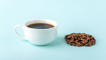 White cup with black coffee espresso and pile of coffee beans on blue background. Caffeine boost morning drink. Close up, minimalism, copy space for text.