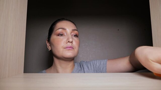 Concentrated tired woman wipes empty wooden shelf with soft orange rag cleaning contemporary walk-in closet at home extreme close view