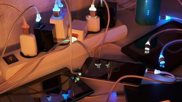 Mobile Phone, power bank and tablets connected to Charging hub on the Table. Extension cord switch loaded with Charger adapters and flashing led USB cables. Recharge gadget concept