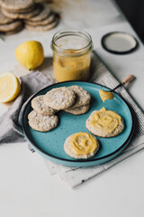 Spreading homemade lemon curd on freshly baked almond cookies on plate. Citrus curd is a traditional English dessert, a creamy paste for tart filling or to spread on biscuits. Home cooking lifestyle.