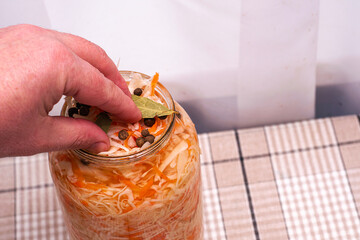 a man puts cabbage in a glass jar for salting with his hands