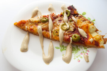 Slice of pizza with olives and sauce on a white plate on a light background