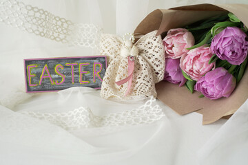 Delicate background with a bouquet of tulips, an angel of lace and a sign with the inscription Easter