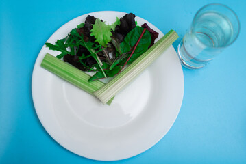 Diet, interval eating, fasting concept. A plate of vegetables depicting a clock, a time slot for a meal. On a blue background.