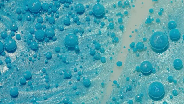 Top view movement of bright oil bubbles in slow motion. Multicolored surface background. Fantastic universe structure of colorful moving blue bubbles. Artistic image of ink drops floating on water