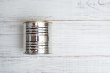 Closed metal can of canned food on a white wooden background.