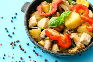 Frying pan with tasty vegetables and chicken on color background, closeup
