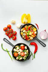 Frying pans with tasty vegetables and chicken on light background