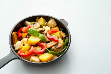 Frying pan with tasty vegetables and chicken on light background