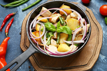 Frying pan with tasty vegetables and chicken on color background