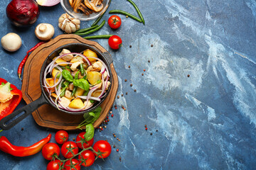 Frying pan with tasty vegetables and chicken on color background
