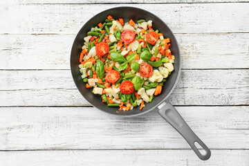 Frying pan with tasty vegetables and chicken on light wooden background