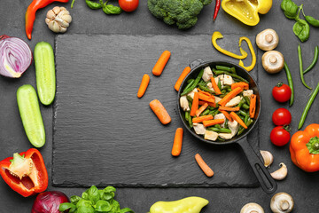 Composition with frying pan, tasty vegetables, chicken and ingredients on dark background