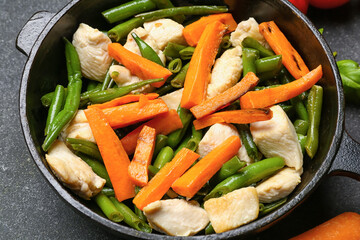 Frying pan with tasty vegetables and chicken on dark background, closeup