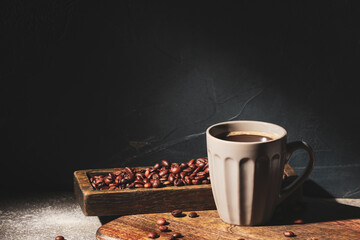Cup of hot coffee and beans on dark background
