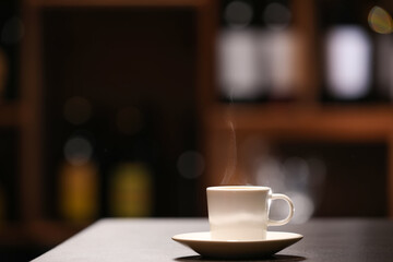 Cup with hot coffee on table against blurred background