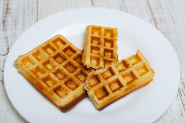 Freshly cooked Belgian waffles on a white plate on a light wooden background.