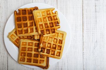 Freshly cooked Belgian waffles on a white plate on a light wooden background.