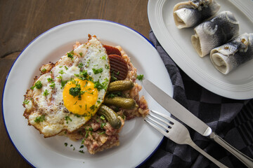 Norddeutscher Hamburger Labskaus mit Rindfleisch Corned Beef, Rote Beete, Kartoffeln, Saure Gurken, Spiegelei und Rollmops auf Emaille Teller