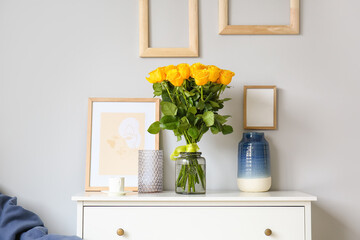 Fototapeta na wymiar Vase with beautiful yellow roses on chest of drawers in interior of room