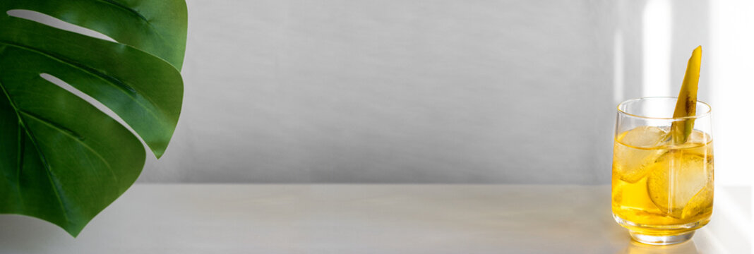 Tropical cocktail decorated with banana slice and ice on large background with palm leaf forn banner. Summer time and vacation concept.