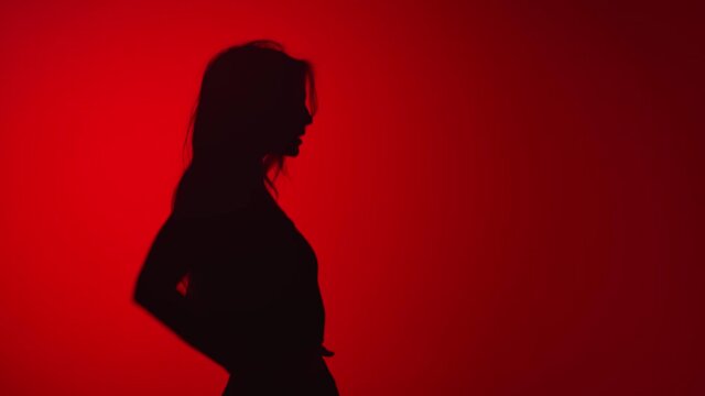 Dark silhouette of cheerful dancing lady having fun isolated red studio. Medium shot on RED camera