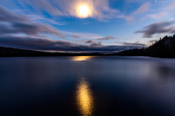 Fototapeta na wymiar vue sur un lac la nuit avec la lumière de la lune qui danse sur le lac