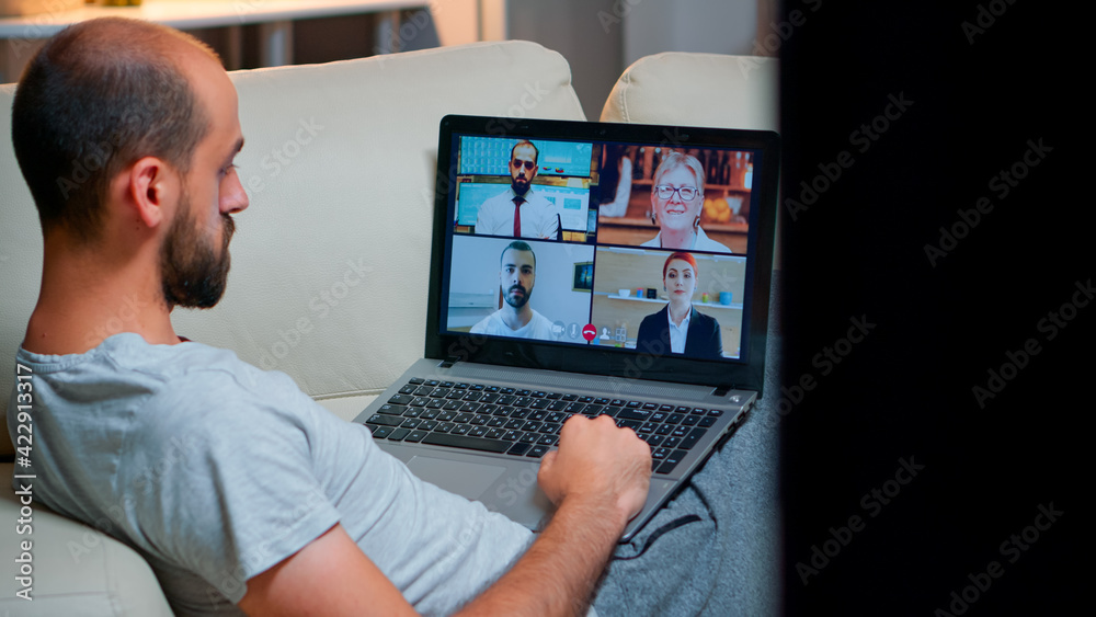 Poster over shoulder view of man in pajamas having online conversation with teammates working at online tec