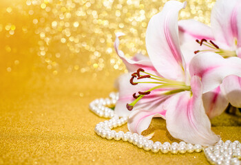 White lilies and pearl necklace on a shiny gold background
