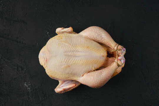 Raw whole broiler chicken with spices on cutting board