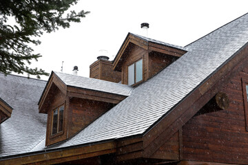 Toit d'un hôtel en bois rond lors de la première neige avec fenêtre